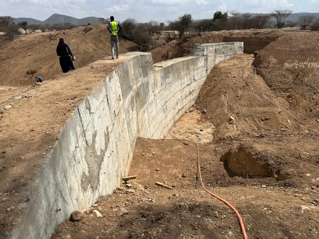 A concrete infrastructure wall under construction in a dry landscape